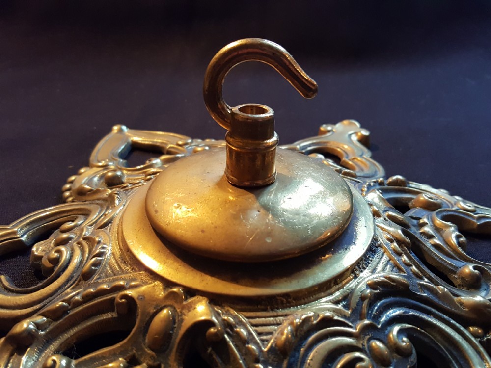 A Victorian cast brass ceiling rose featuring a central metal hook surrounded by openwork scrollwork and a starburst edge profile. View III
