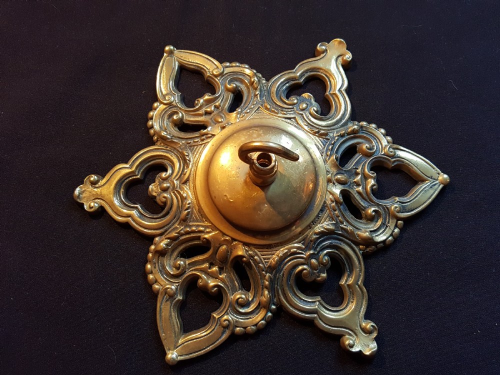 A Victorian cast brass ceiling rose featuring a central metal hook surrounded by openwork scrollwork and a starburst edge profile. View IV