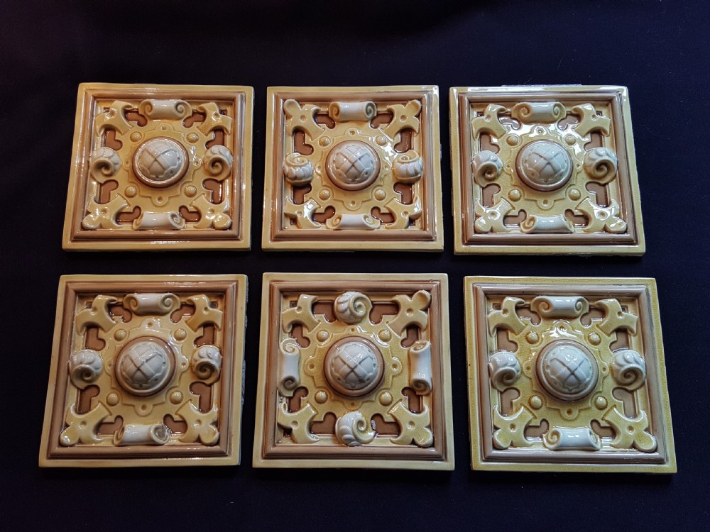 A set of six Victorian square earthenware tiles featuring high-relief moulded scrollwork and central cabochons in ochre and brown glazes.