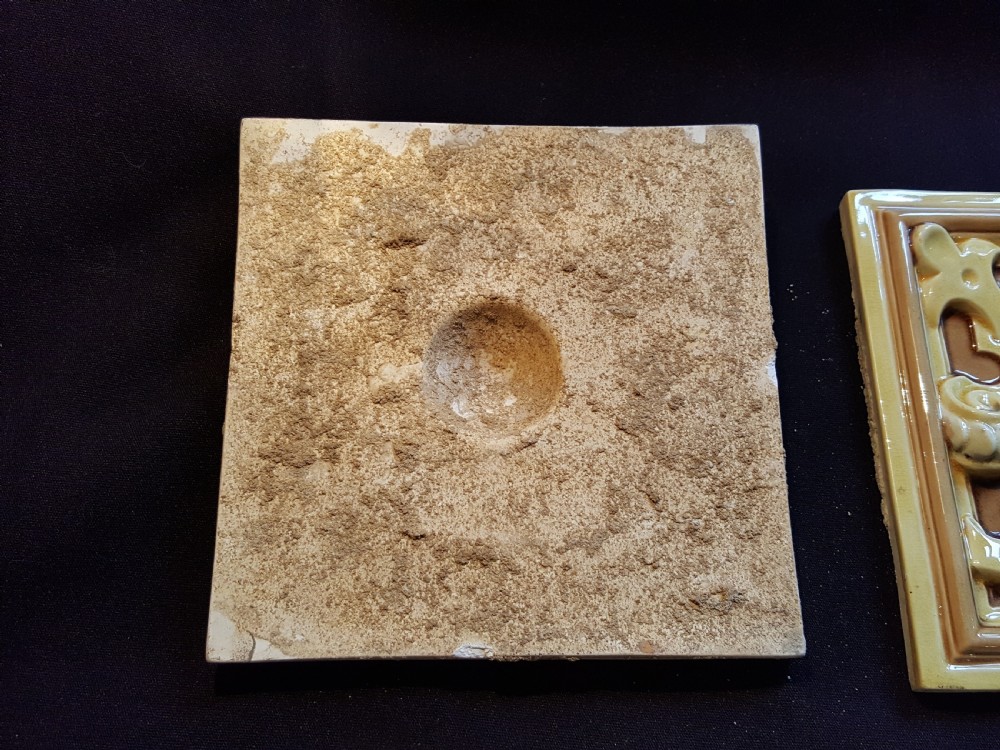 A set of six Victorian square earthenware tiles featuring high-relief moulded scrollwork and central cabochons in ochre and brown glazes. View VI