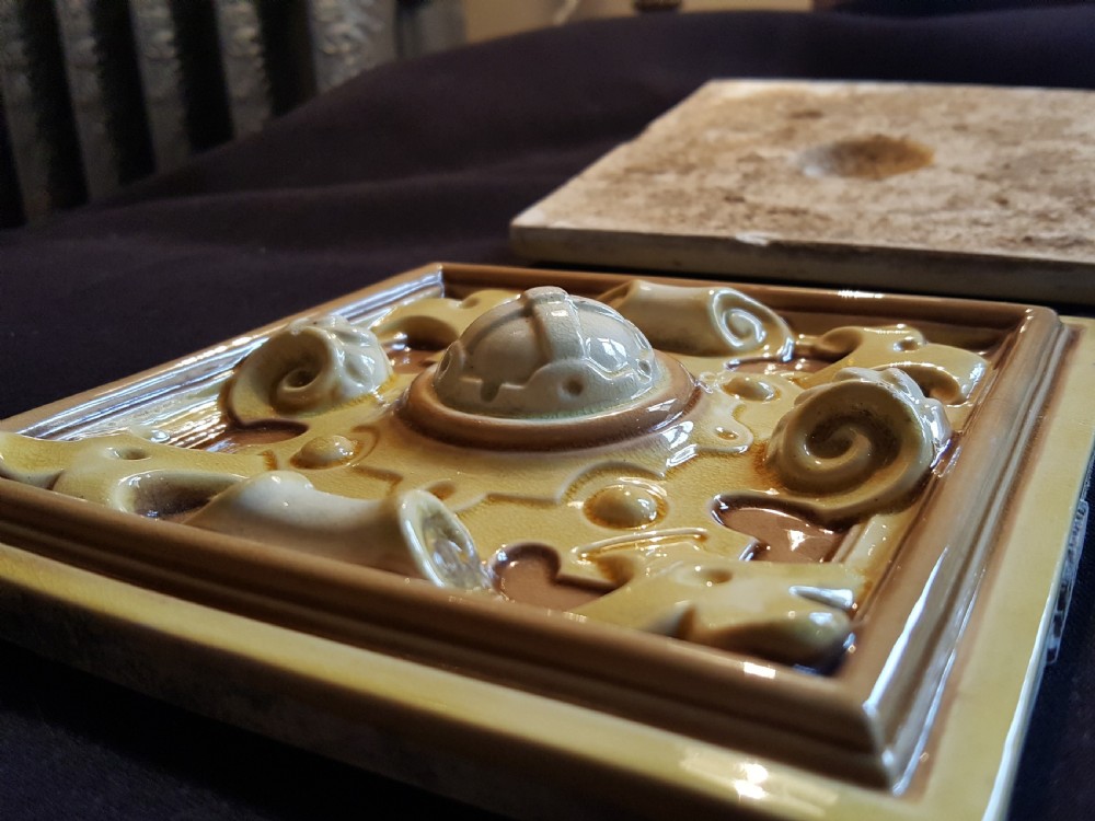 A set of six Victorian square earthenware tiles featuring high-relief moulded scrollwork and central cabochons in ochre and brown glazes. View X