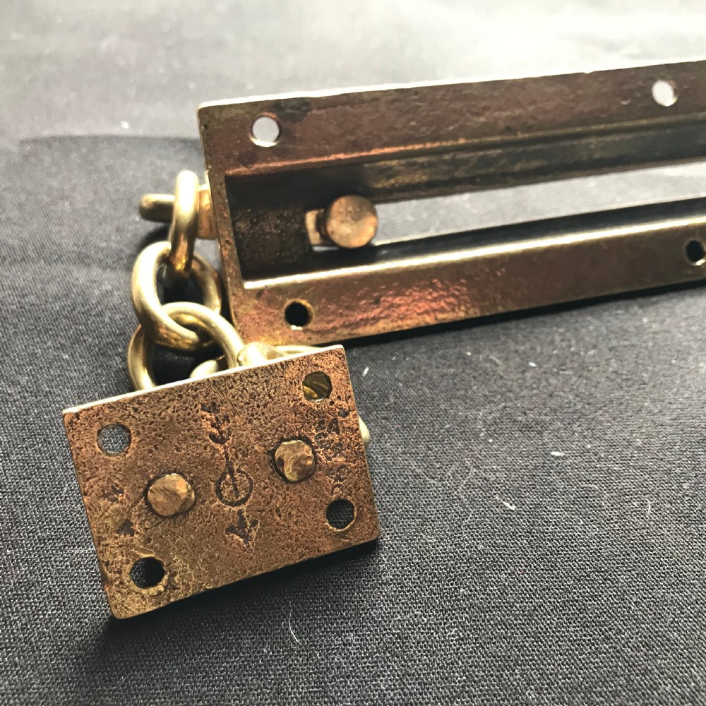 A solid brass Victorian night door chain featuring a slotted slider backplate, a small mounting plate, and connecting oval chain links. View V