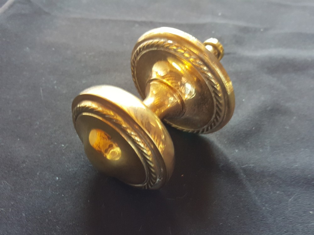 A solid brass Regency centre door knob featuring a circular domed face with a rope-twist border and matching backplate.