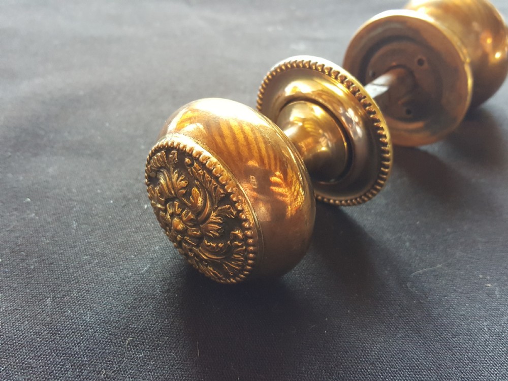 A pair of polished Regency brass door knobs joined by a square spindle, featuring beaded rims and central floral relief details. View II