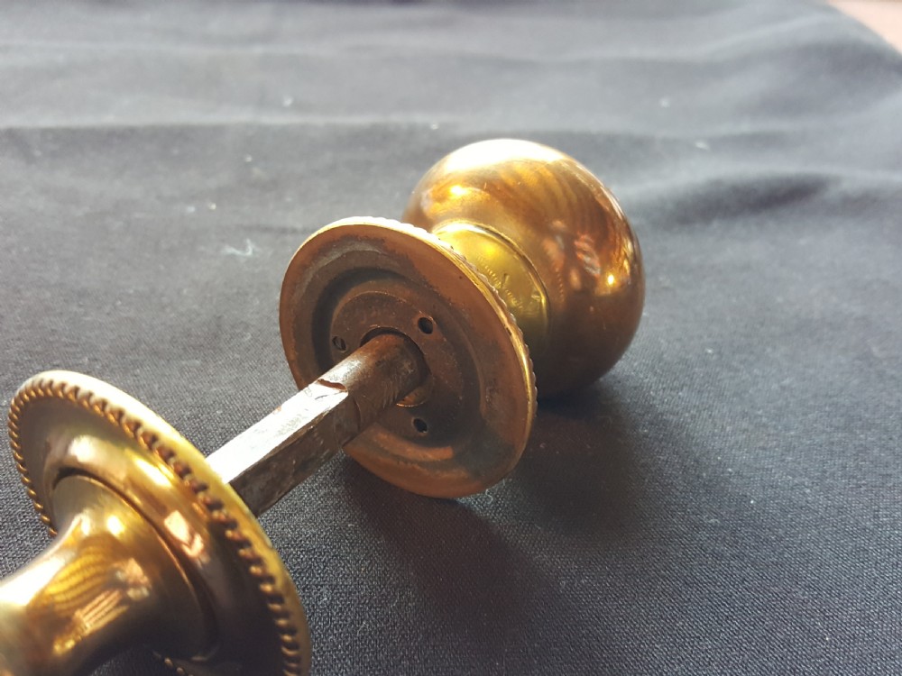 A pair of polished Regency brass door knobs joined by a square spindle, featuring beaded rims and central floral relief details. View III