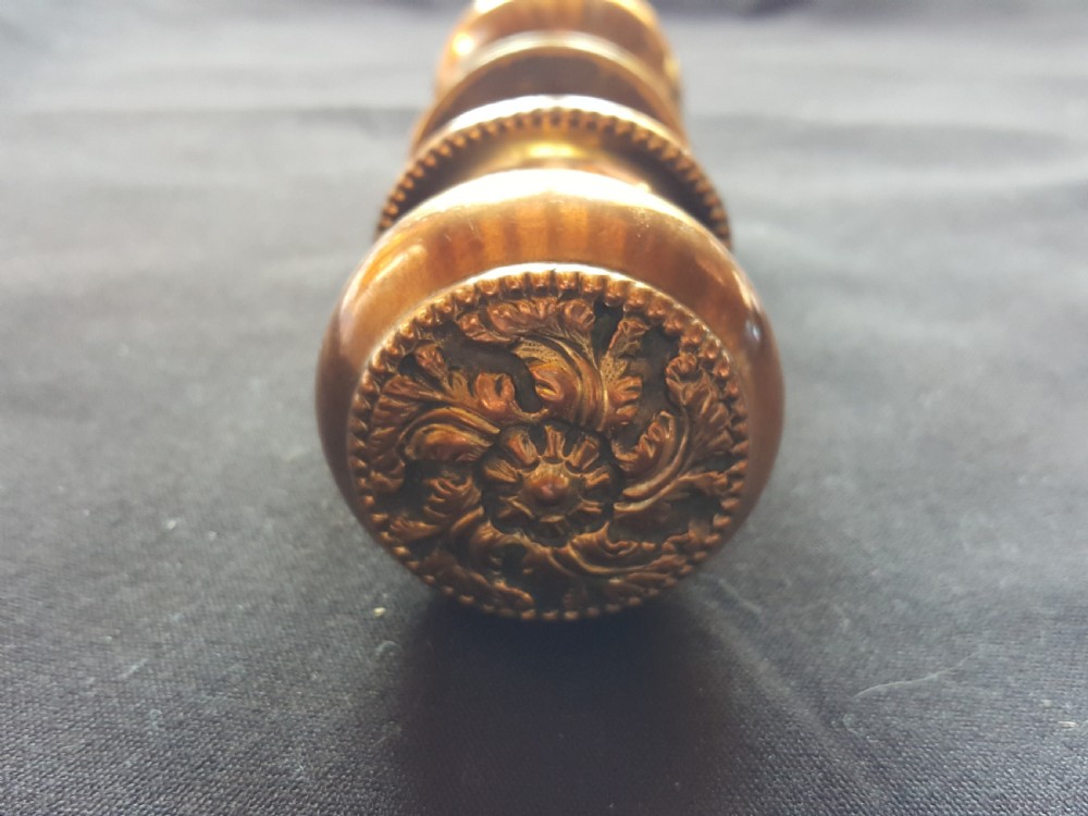 A pair of polished Regency brass door knobs joined by a square spindle, featuring beaded rims and central floral relief details. View V