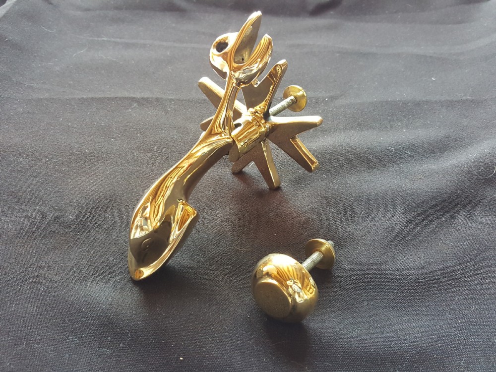 A polished brass door knocker shaped as a stylised dolphin mounted on a Maltese cross backplate alongside a separate brass striker button.