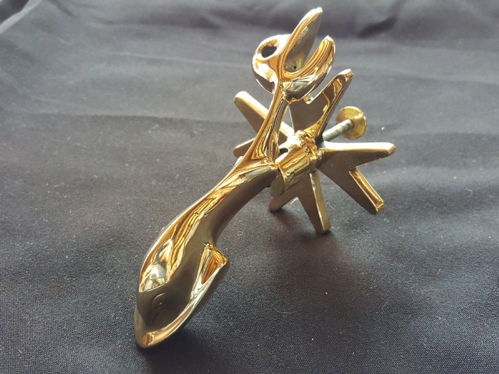 A polished brass door knocker shaped as a stylised dolphin mounted on a Maltese cross backplate alongside a separate brass striker button. View II