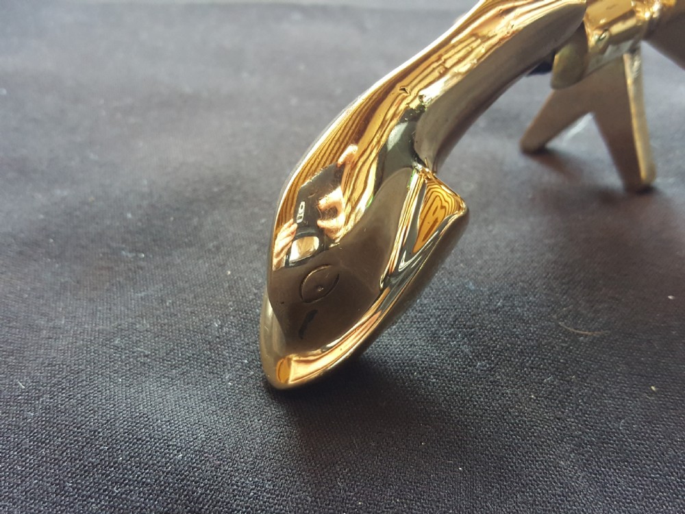 A polished brass door knocker shaped as a stylised dolphin mounted on a Maltese cross backplate alongside a separate brass striker button. View III