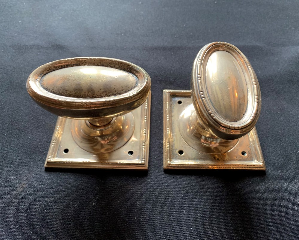 A pair of antique cast bronze oval door knobs mounted on square backplates with beaded borders.