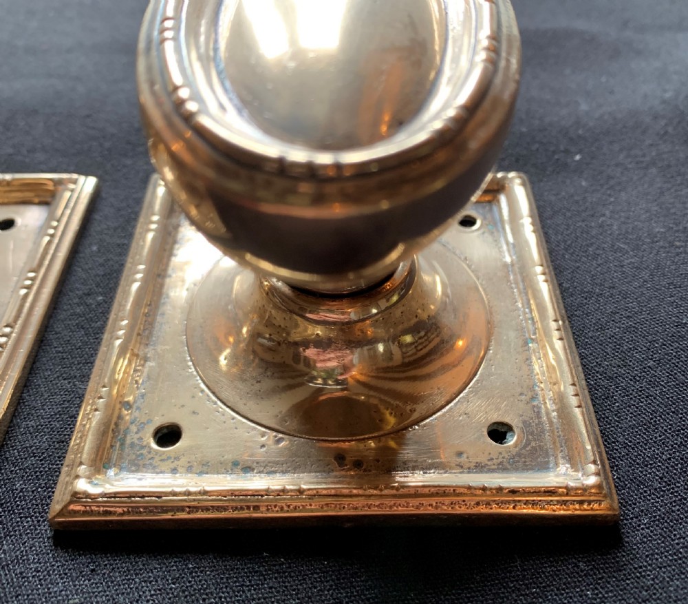 A pair of antique cast bronze oval door knobs mounted on square backplates with beaded borders. View V