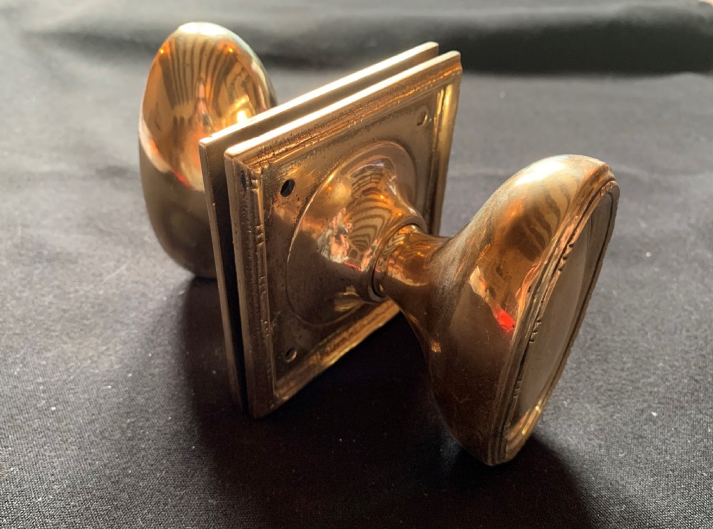 A pair of antique cast bronze oval door knobs mounted on square backplates with beaded borders. View VII