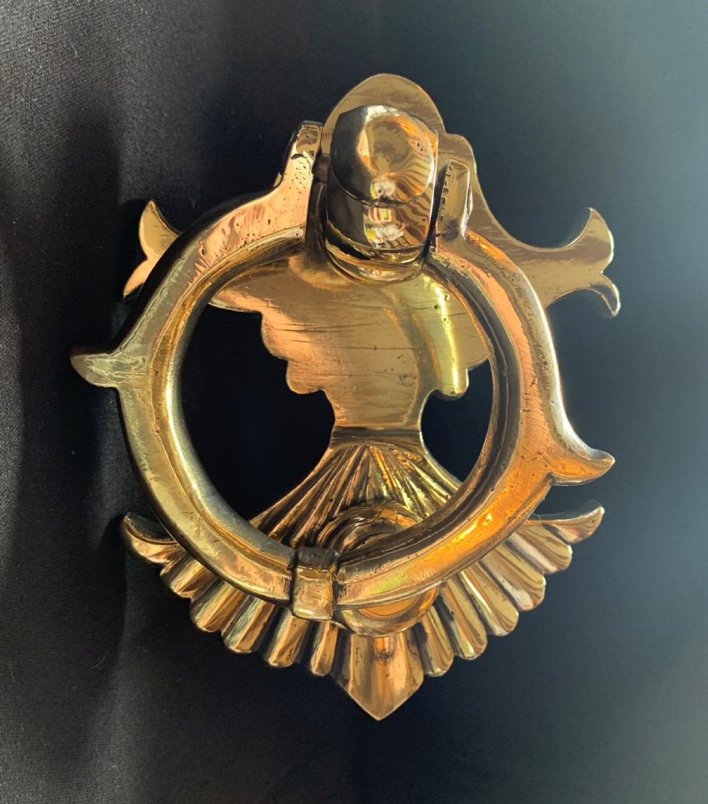 A polished solid brass Victorian door knocker featuring a heavy circular ring hinged above a fluted fan backplate.