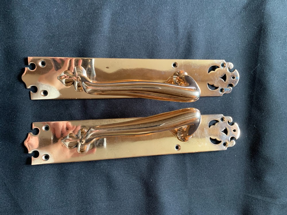 A pair of polished bronze Art Nouveau door pull handles mounted on rectangular backplates with decorative cutouts and floral base motifs. View II