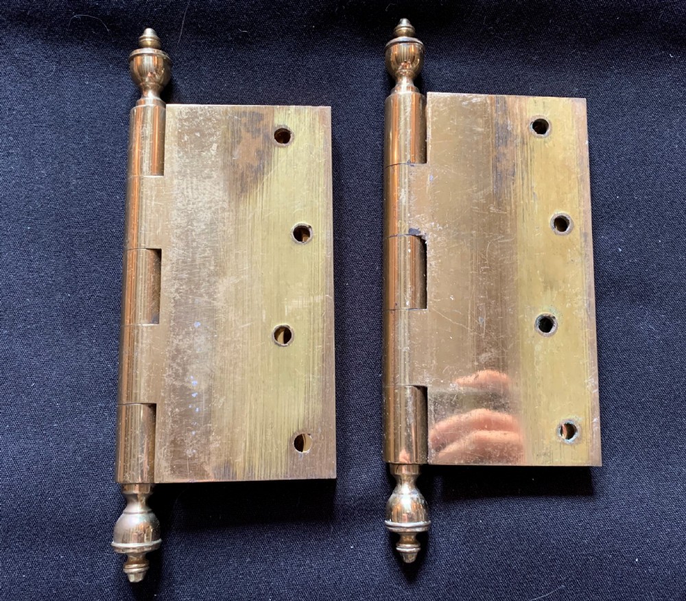 A pair of solid brass Victorian door hinges featuring decorative turned finials at both ends of each hinge pin.