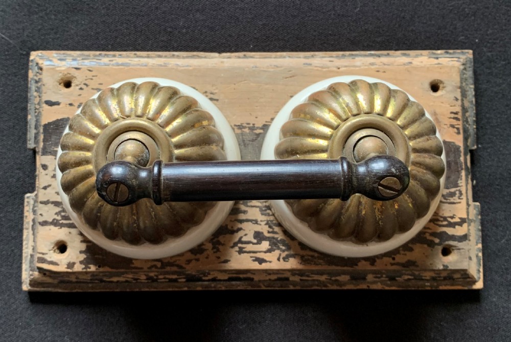 An antique Victorian double lever light switch featuring fluted brass domes on white porcelain bases, connected by a dark wooden lever bar on a timber backplate. View II