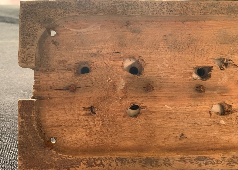 An antique Victorian double lever light switch featuring fluted brass domes on white porcelain bases, connected by a dark wooden lever bar on a timber backplate. View V
