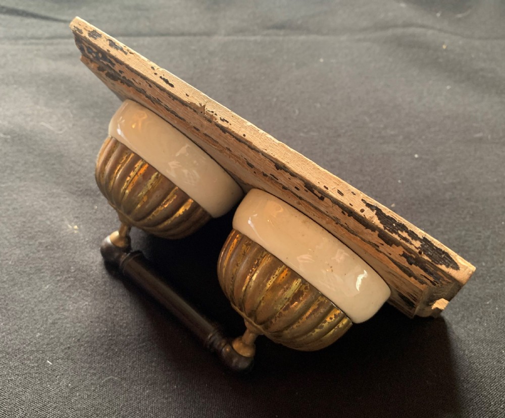 An antique Victorian double lever light switch featuring fluted brass domes on white porcelain bases, connected by a dark wooden lever bar on a timber backplate. View VII
