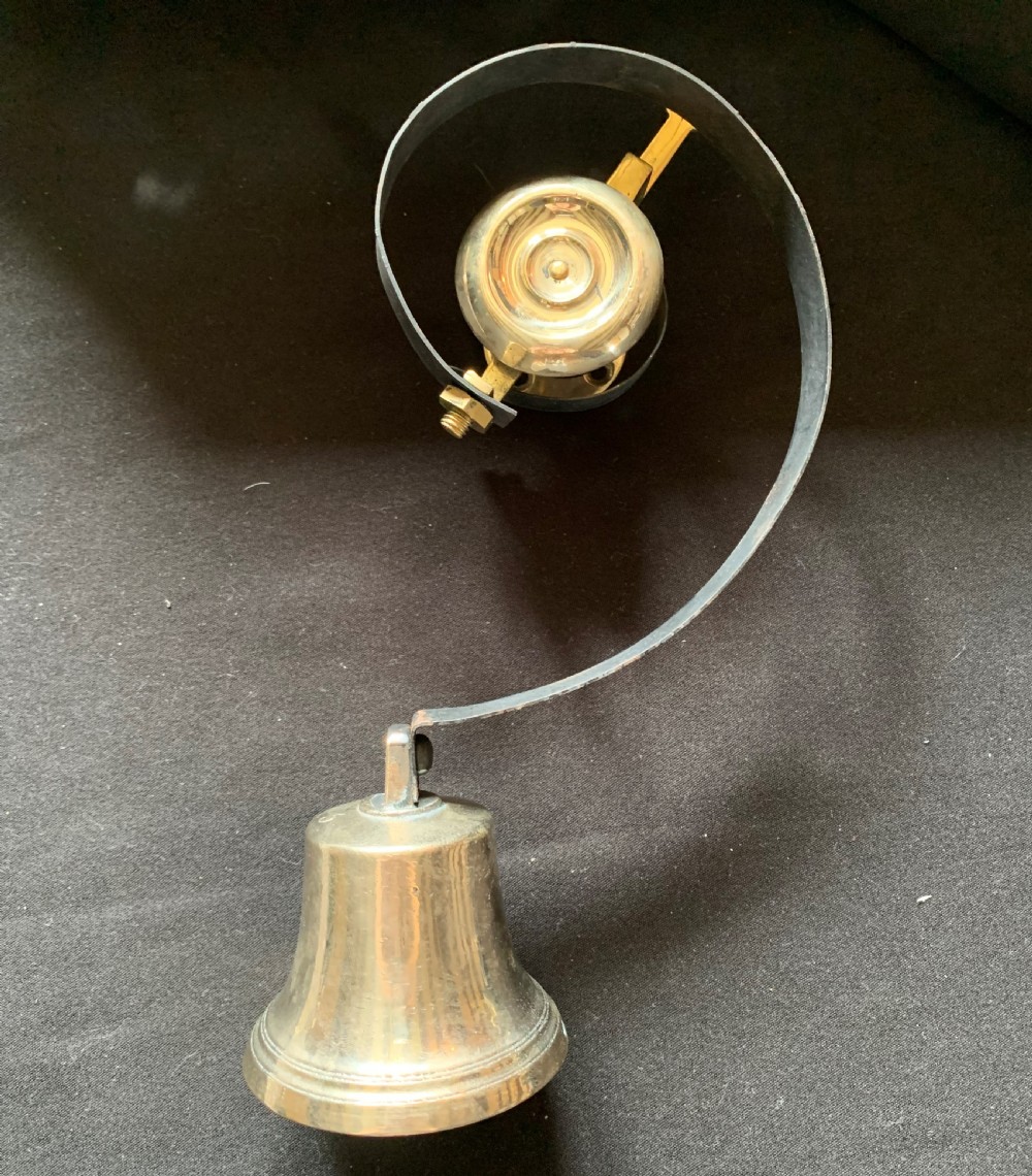 A restored Victorian mechanical servants bell featuring a polished brass bell suspended from a curved black steel spiral spring.