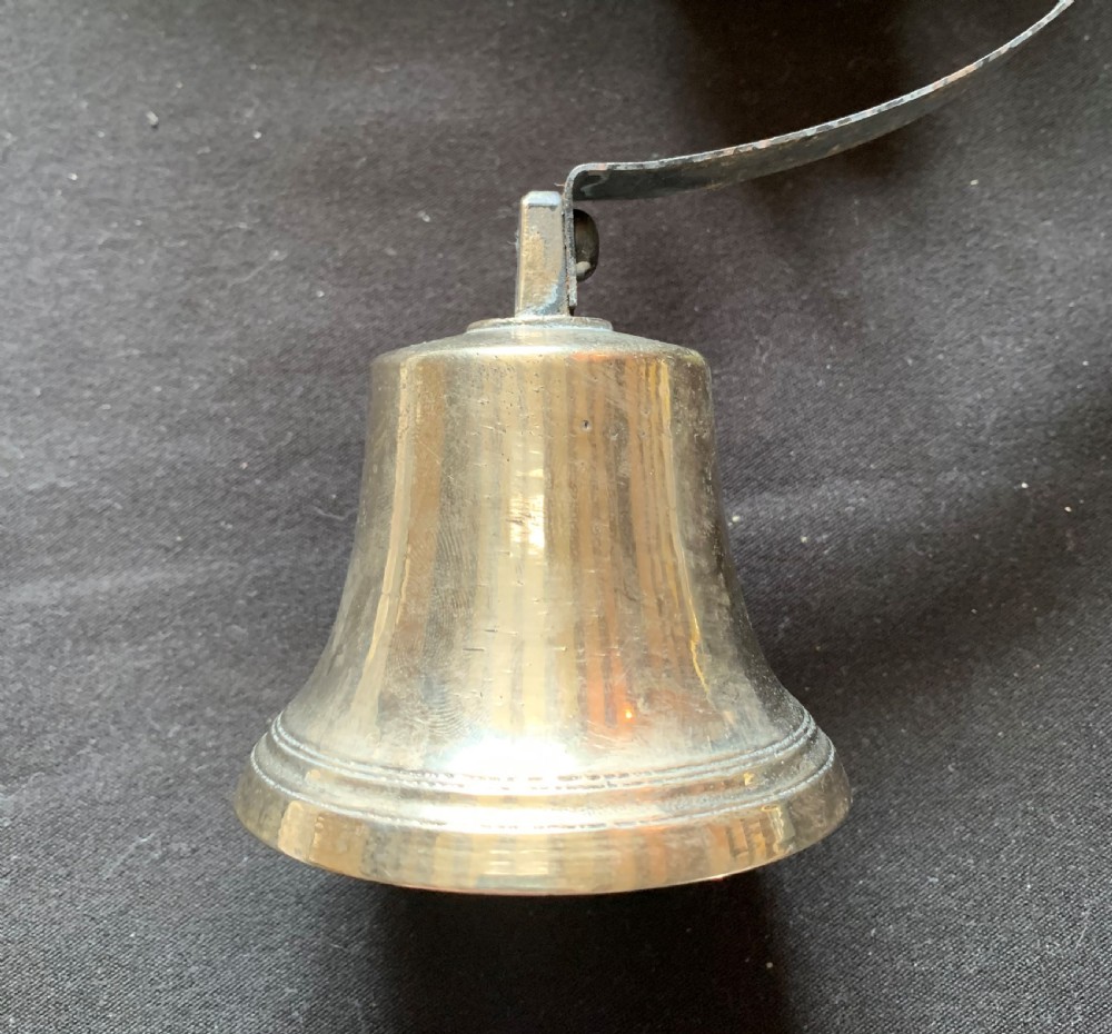 A restored Victorian mechanical servants bell featuring a polished brass bell suspended from a curved black steel spiral spring. View II