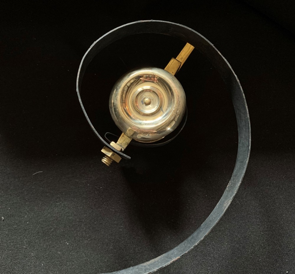 A restored Victorian mechanical servants bell featuring a polished brass bell suspended from a curved black steel spiral spring. View III