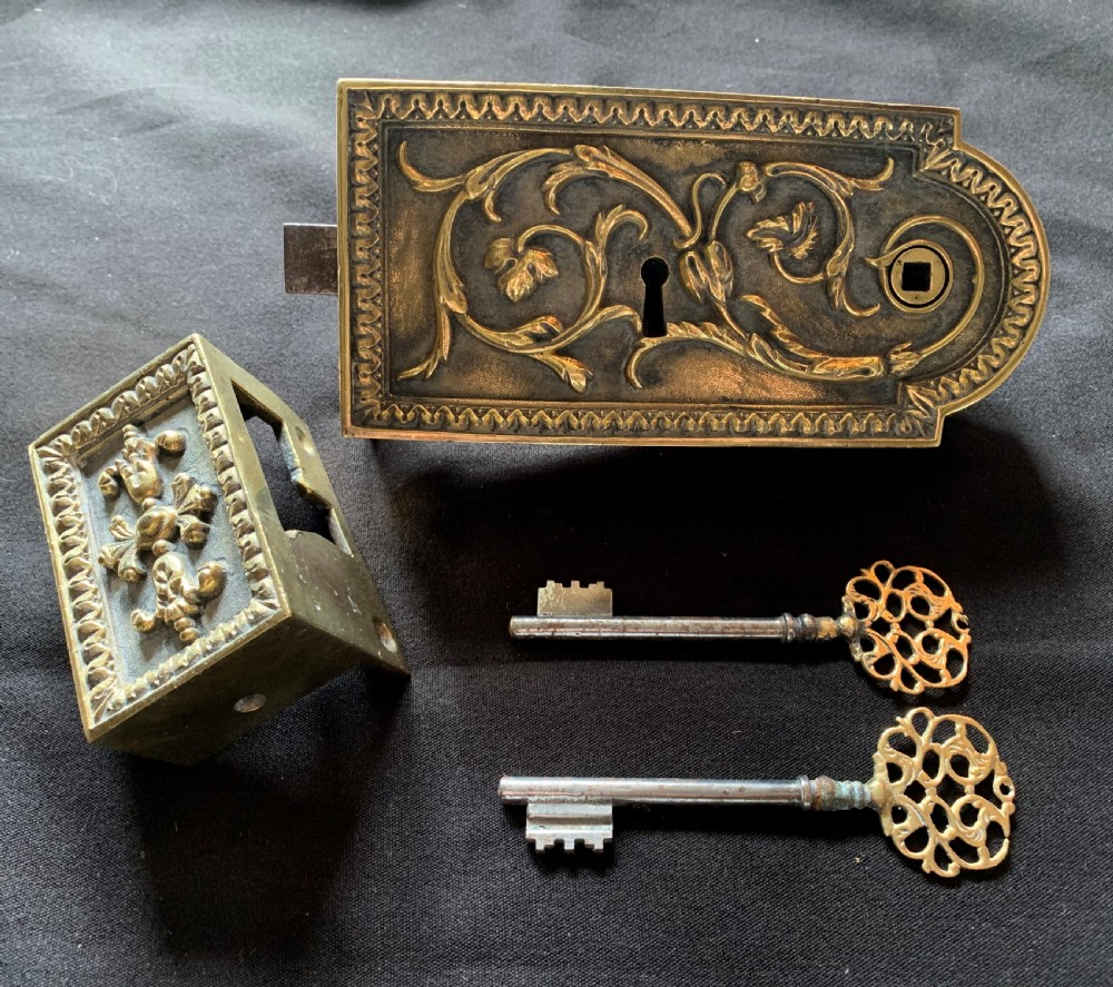 An ornate French Victorian brass rim lock set featuring raised foliate scrollwork, a matching keep, and two decorative keys.