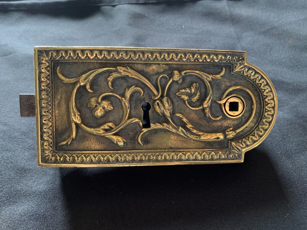 An ornate French Victorian brass rim lock set featuring raised foliate scrollwork, a matching keep, and two decorative keys. View III
