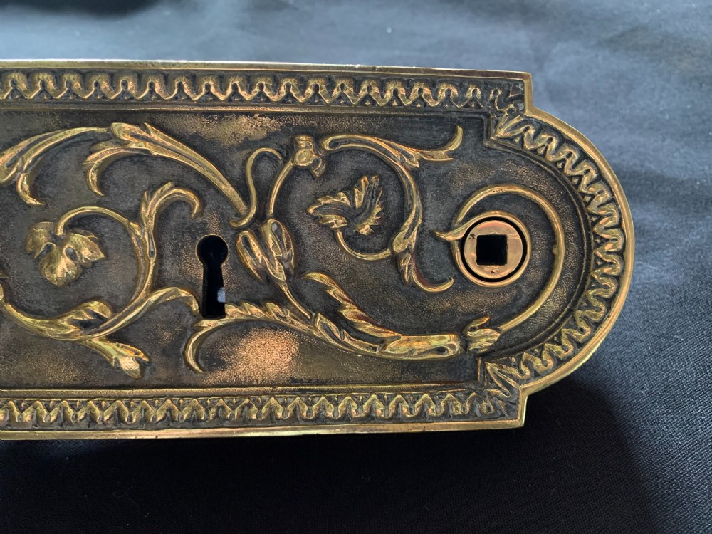 An ornate French Victorian brass rim lock set featuring raised foliate scrollwork, a matching keep, and two decorative keys. View V