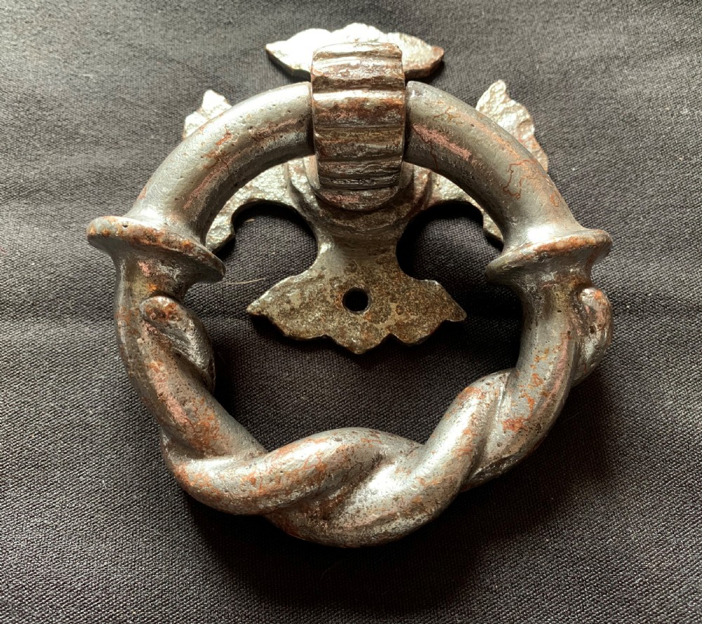 A dark cast iron door knocker featuring a twisted ring handle suspended from a decorative gothic mounting plate. View II