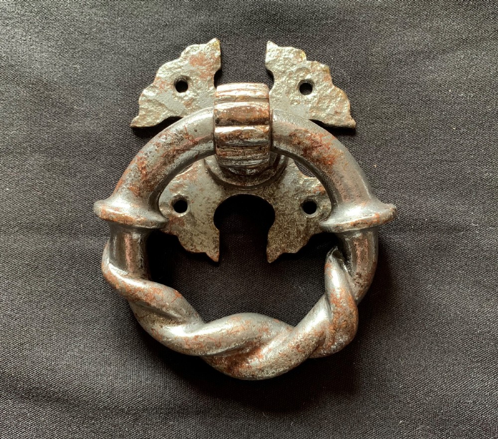 A dark cast iron door knocker featuring a twisted ring handle suspended from a decorative gothic mounting plate. View III