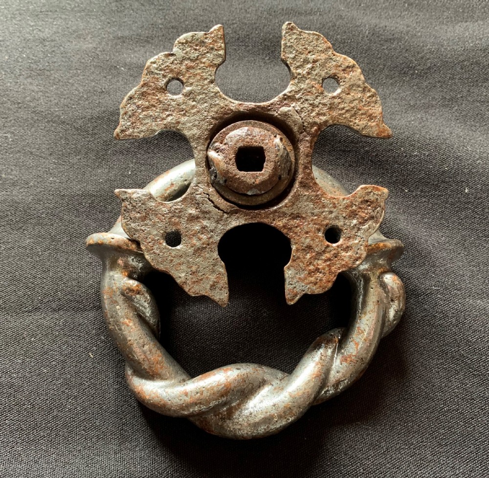 A dark cast iron door knocker featuring a twisted ring handle suspended from a decorative gothic mounting plate. View IV