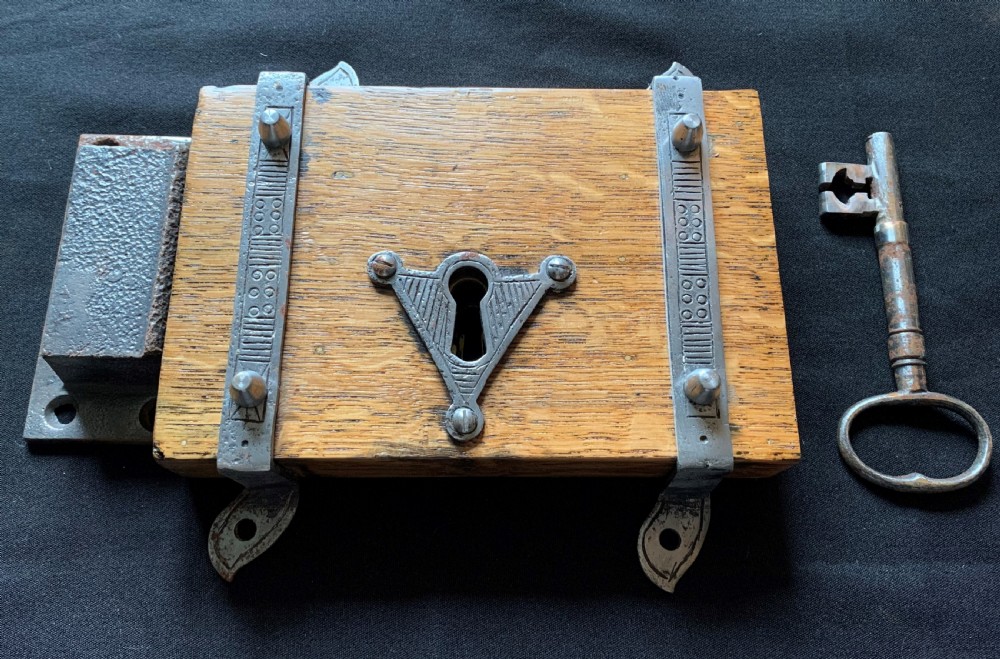 An antique Victorian surface-mounted wooden rim lock crafted from oak with decorative steel straps, accompanied by a steel keep and an original iron key.