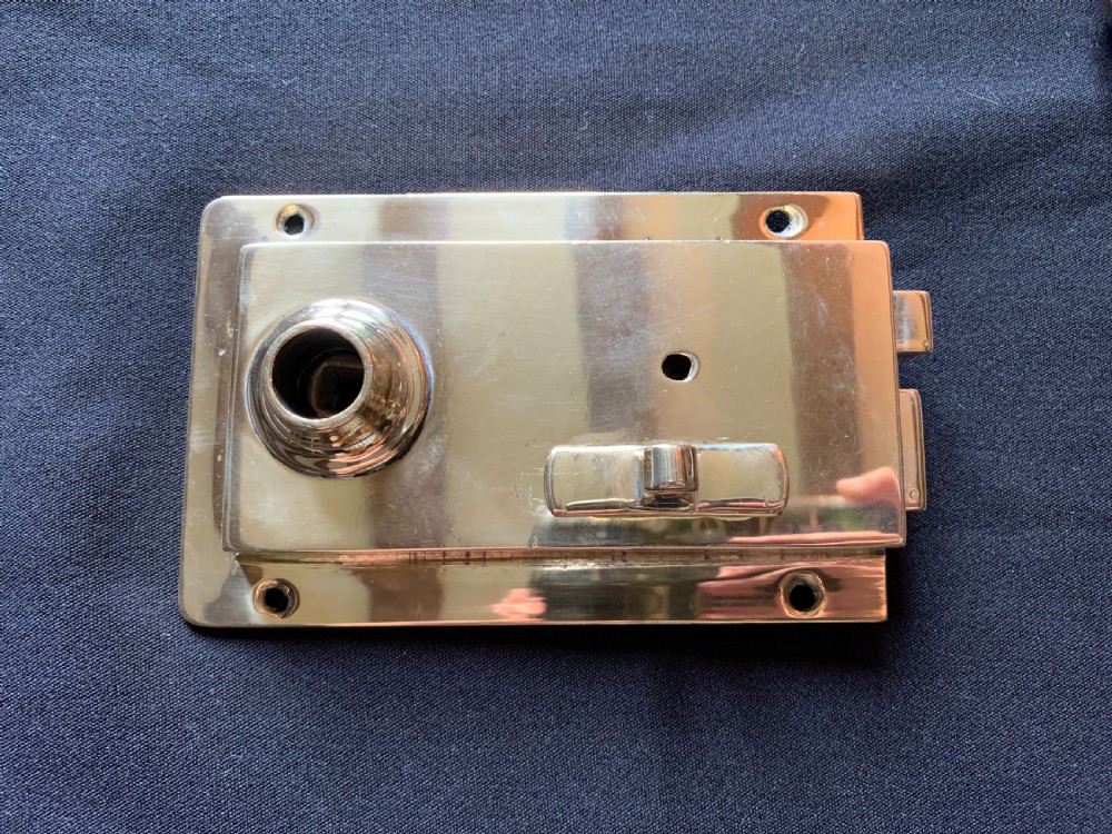 A polished brass Art Nouveau rim lock set featuring a rectangular surface lock, matching keep plate, and a pair of round fluted brass door knobs on a spindle. View II