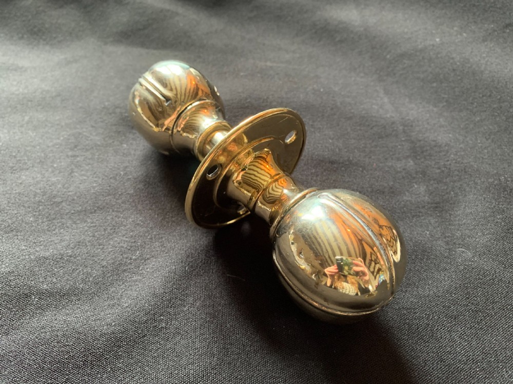 A polished brass Art Nouveau rim lock set featuring a rectangular surface lock, matching keep plate, and a pair of round fluted brass door knobs on a spindle. View III