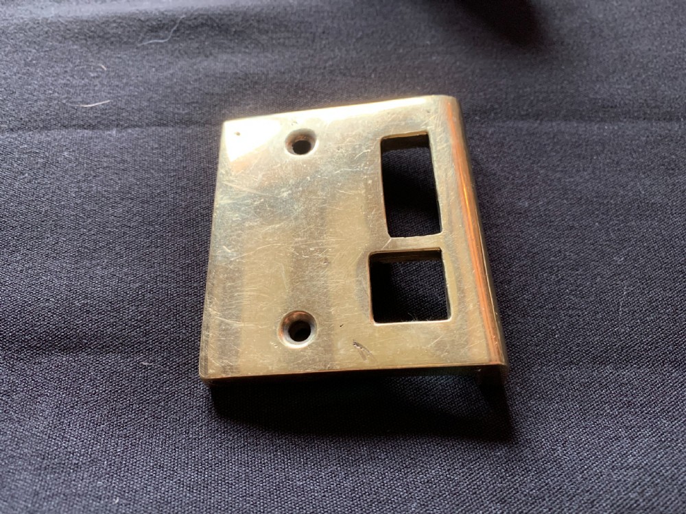 A polished brass Art Nouveau rim lock set featuring a rectangular surface lock, matching keep plate, and a pair of round fluted brass door knobs on a spindle. View V