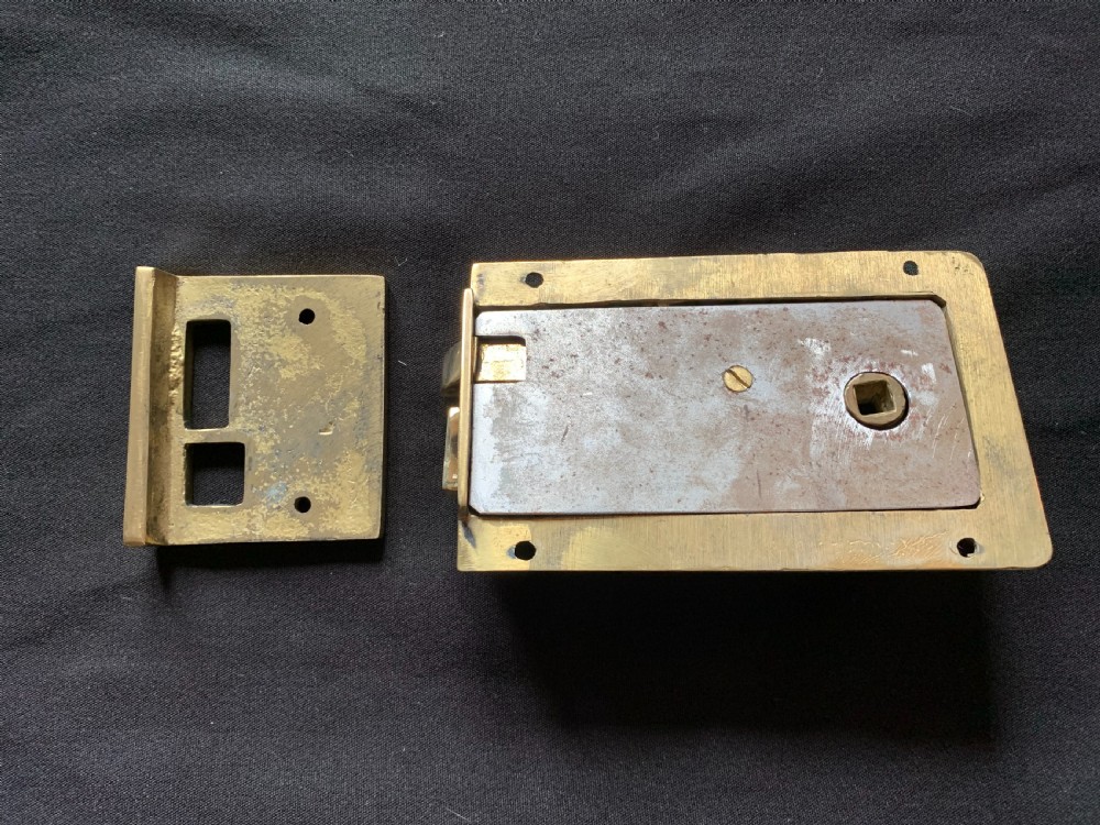 A polished brass Art Nouveau rim lock set featuring a rectangular surface lock, matching keep plate, and a pair of round fluted brass door knobs on a spindle. View VI