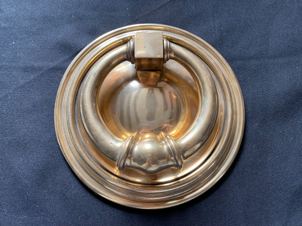 A circular polished brass Georgian door knocker with a heavy ring handle mounted on a moulded circular backplate.