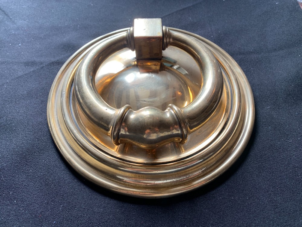 A circular polished brass Georgian door knocker with a heavy ring handle mounted on a moulded circular backplate. View II