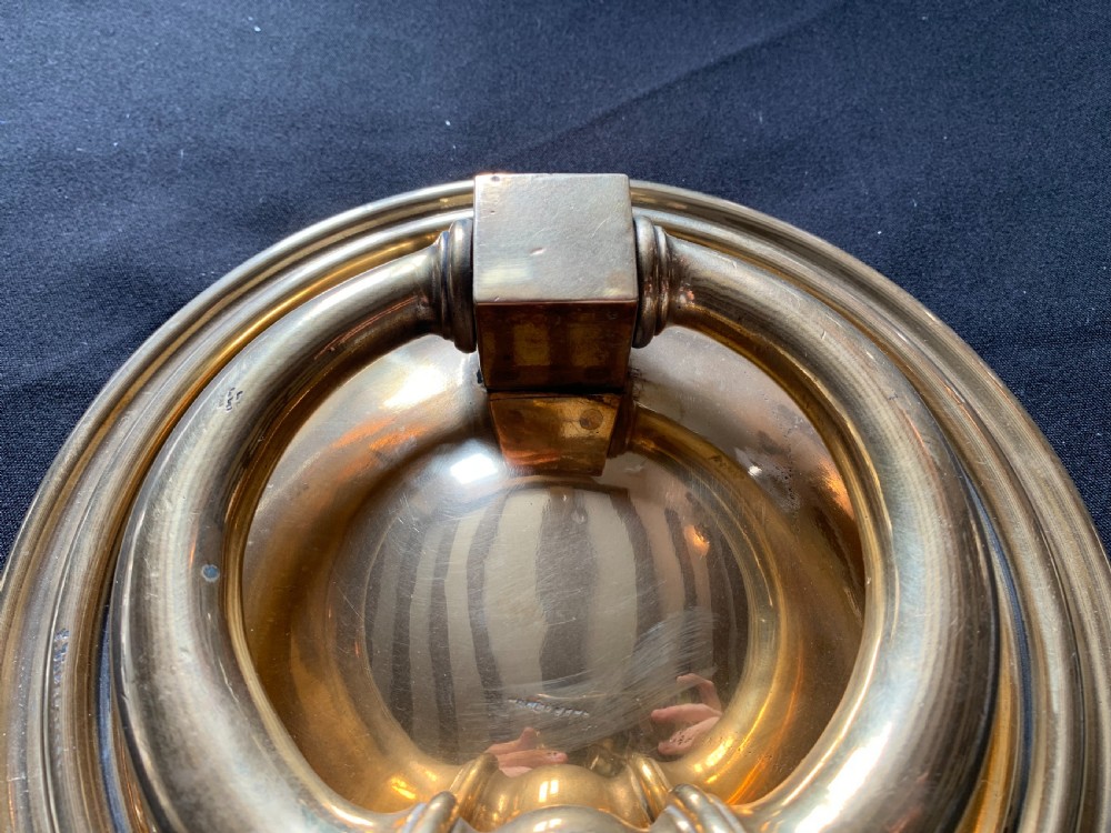 A circular polished brass Georgian door knocker with a heavy ring handle mounted on a moulded circular backplate. View IV