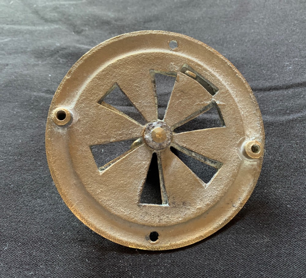 A circular solid brass Victorian hit-and-miss air vent with a central turning handle, triangular slotted openings, and two mounting screw holes. View IV