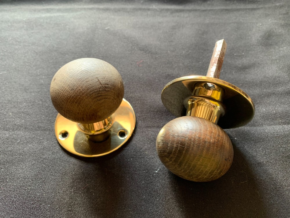 A pair of turned wooden door knobs featuring polished brass stems and circular backplates, shown with an iron connecting spindle.