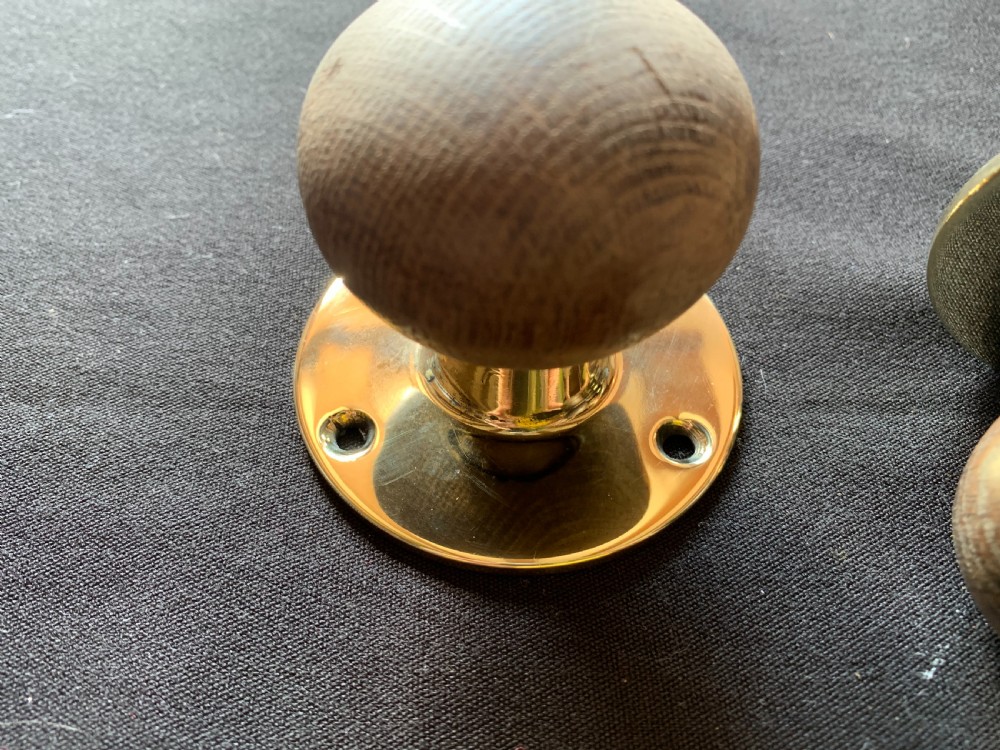 A pair of turned wooden door knobs featuring polished brass stems and circular backplates, shown with an iron connecting spindle. View III