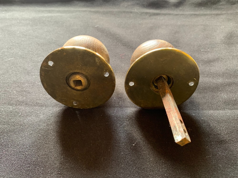 A pair of turned wooden door knobs featuring polished brass stems and circular backplates, shown with an iron connecting spindle. View V