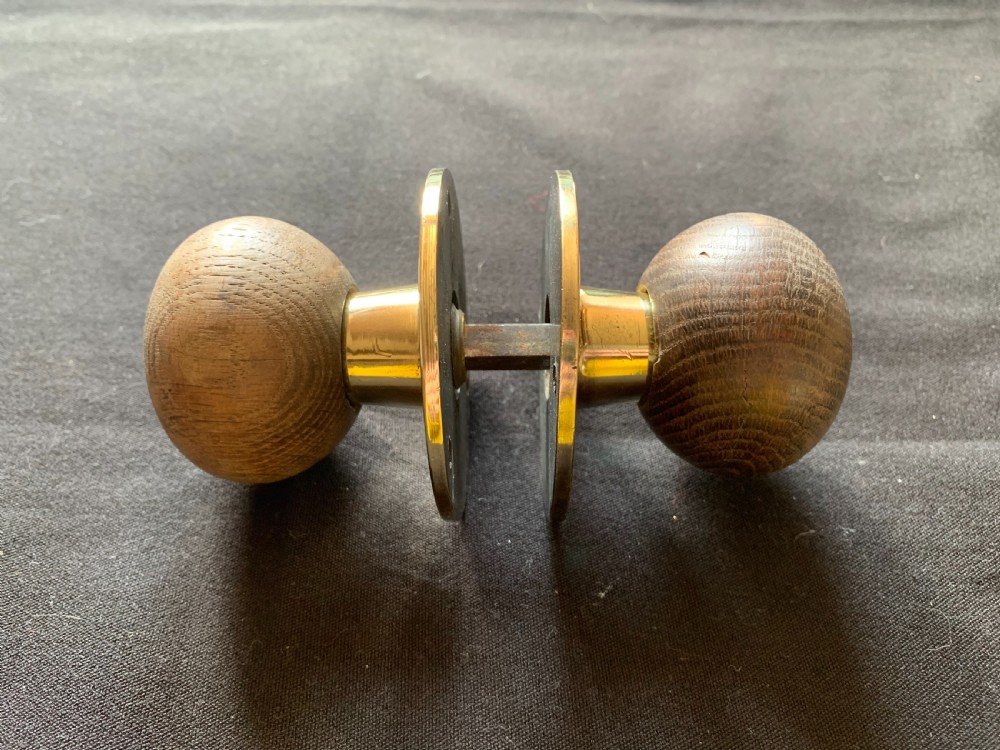 A pair of turned wooden door knobs featuring polished brass stems and circular backplates, shown with an iron connecting spindle. View VI