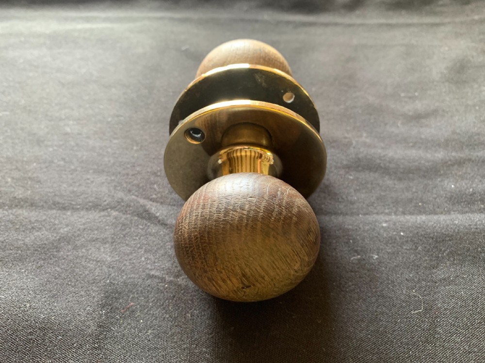 A pair of turned wooden door knobs featuring polished brass stems and circular backplates, shown with an iron connecting spindle. View VII