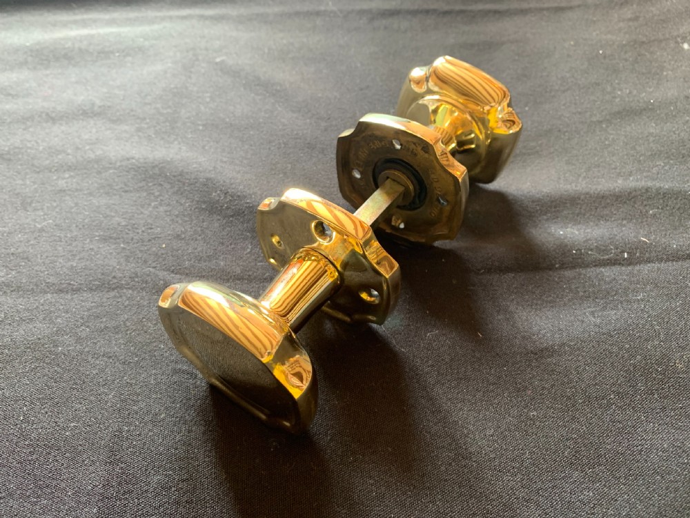 A pair of polished brass Victorian door knobs with square rose plates and a connecting spindle.