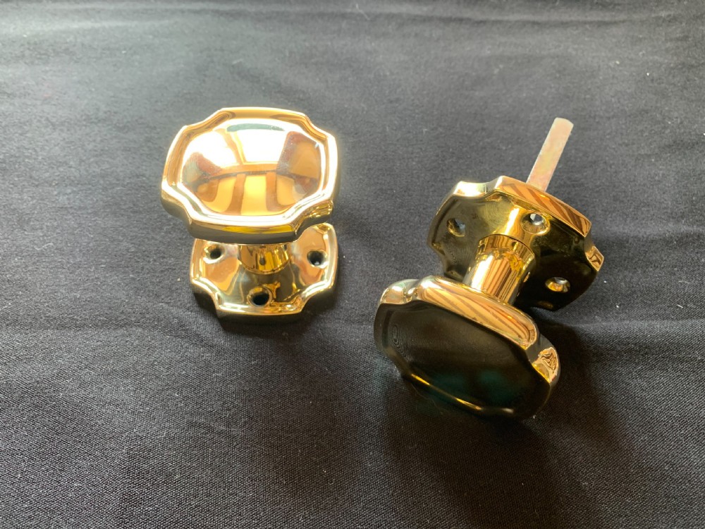 A pair of polished brass Victorian door knobs with square rose plates and a connecting spindle. View II
