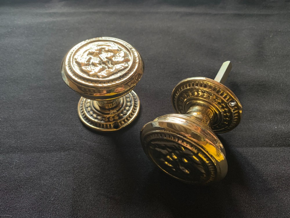 A pair of polished brass Victorian door knobs featuring raised embossed circular patterns and matching backplates.