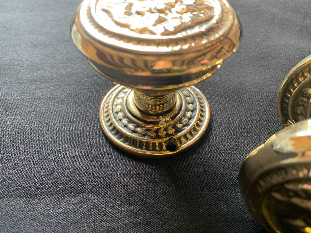 A pair of polished brass Victorian door knobs featuring raised embossed circular patterns and matching backplates. View V