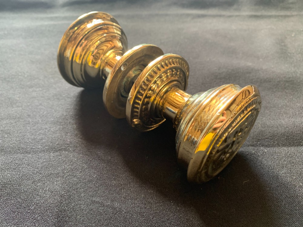 A pair of polished brass Victorian door knobs featuring raised embossed circular patterns and matching backplates. View VI